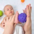 Mom gives baby foot massage with purple rubber ball. Selective focus